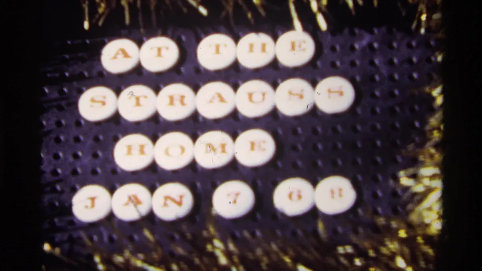 Close 1968 home-movie view of the circular tiles reading “AT THE STRAUSS HOME JAN 7 68” beside gold holiday tinsel.