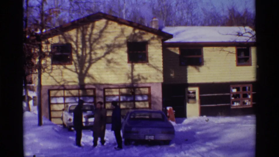 In Chicago home-movie footage from 1968, three men stand in winter coats outside a yellow-sided house beside two parked cars.