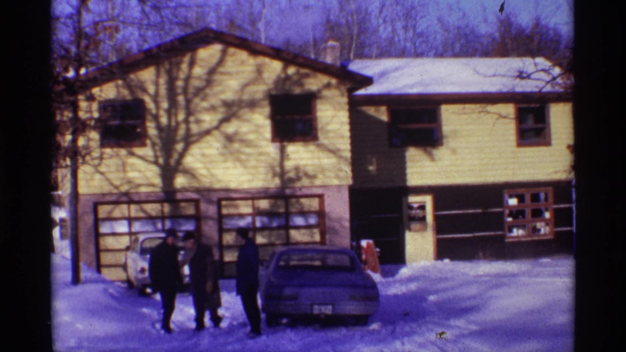 Three men in dark winter coats move casually near parked cars outside a yellow-sided Chicago residence in 1968 home-movie footage.