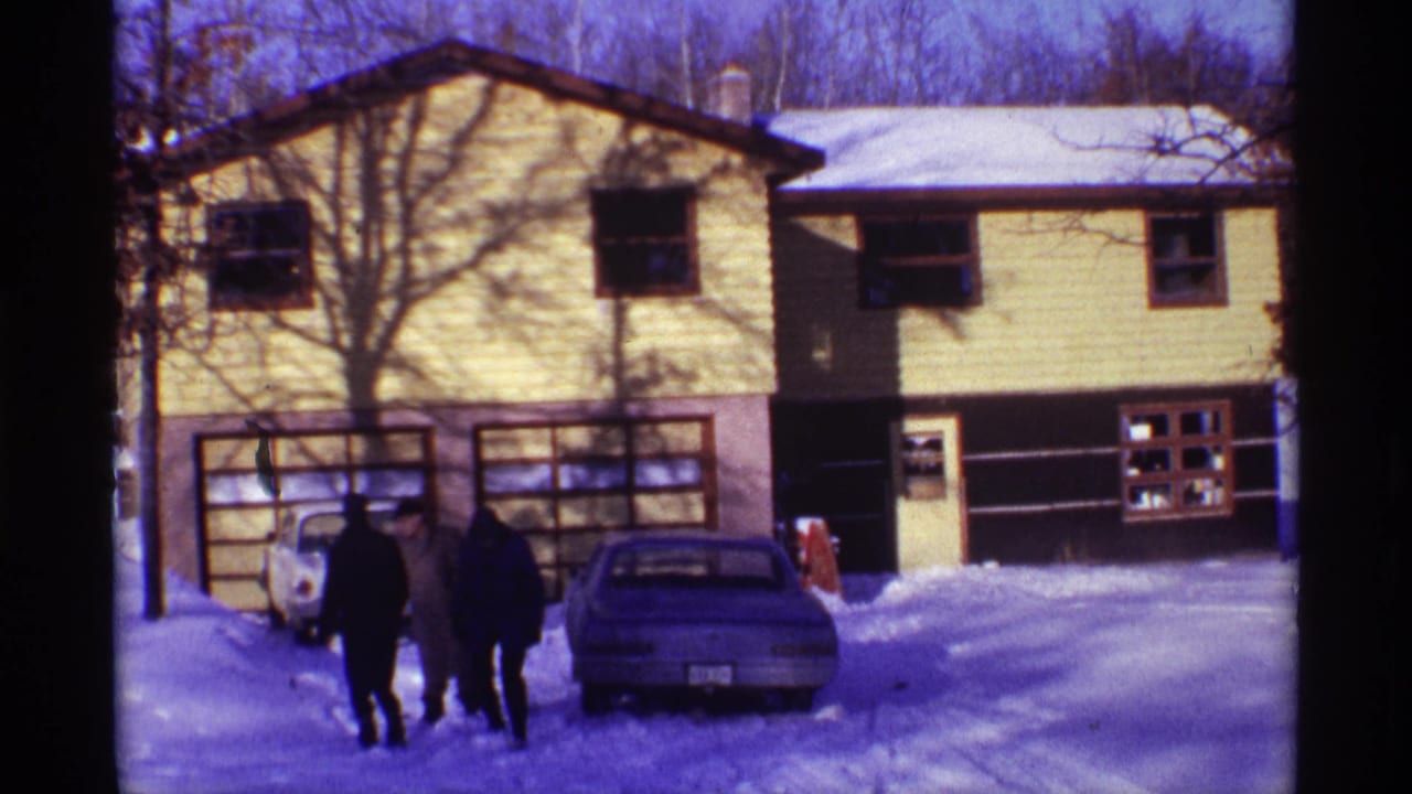 Yellow house and parked cars beside people walking through deep snow.