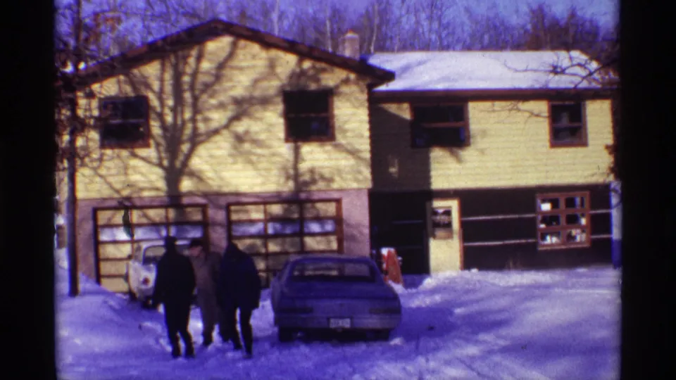 1968 Chicago home-movie frame showing a yellow-sided house, driveway cars, and bundled people moving through snow.
