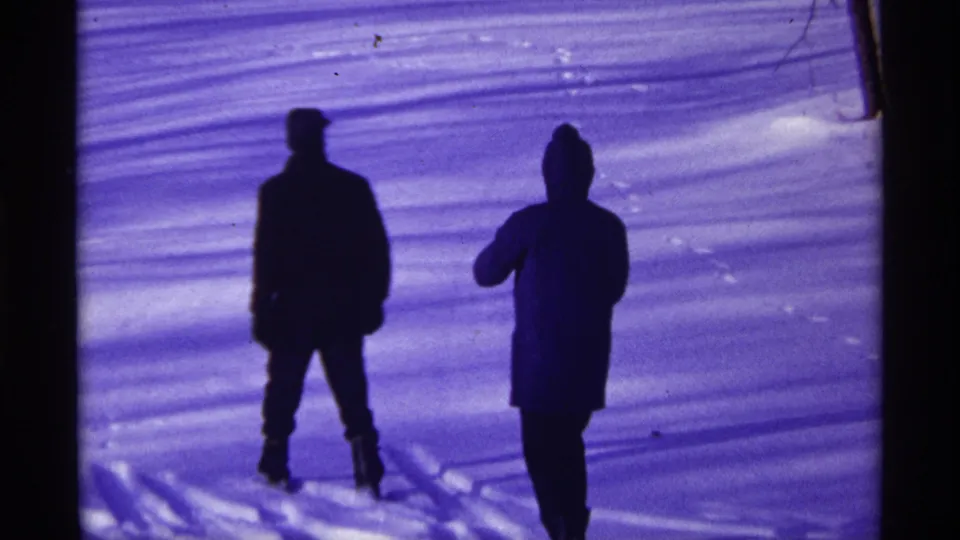Two people in winter coats stand or walk across bright snow in a 1968 Chicago home-movie scene.