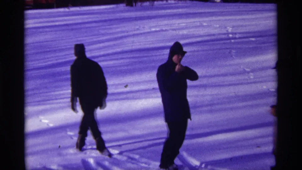Two bundled figures move across a snowy Chicago yard, with one person turning near the camera in winter clothing.