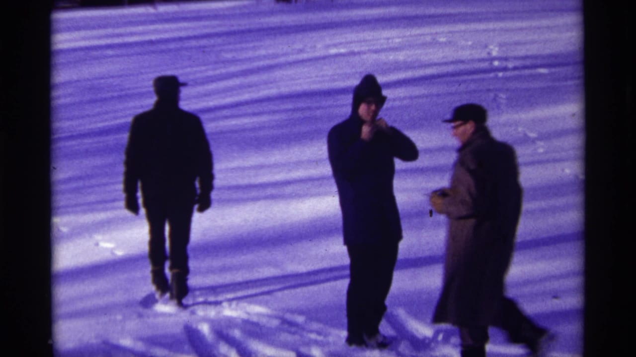 Three bundled men stand on bright snow near long shadows.