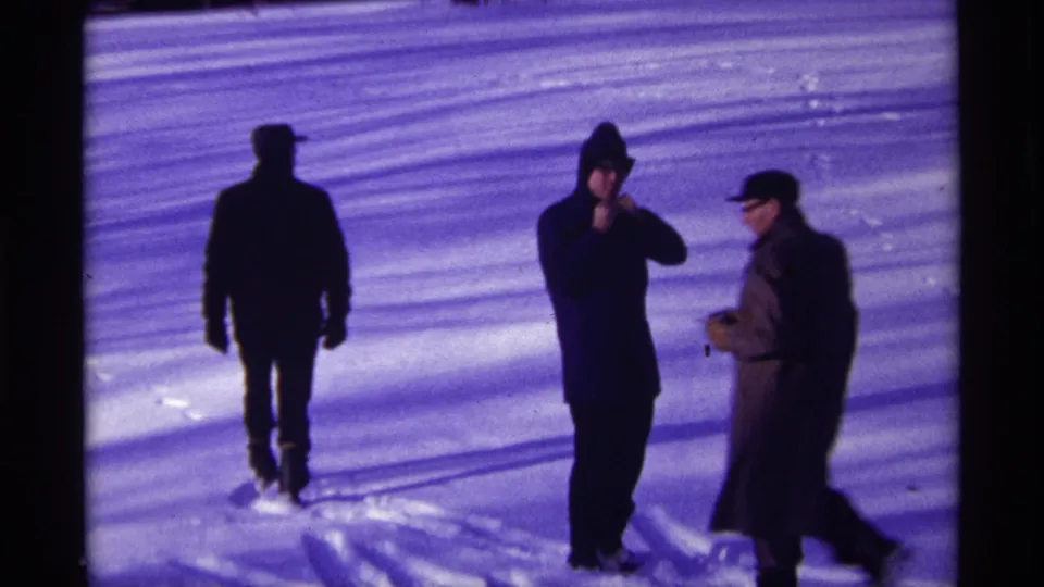 Three men in dark winter coats and hats stand on snow in 1968 Chicago home-movie footage.
