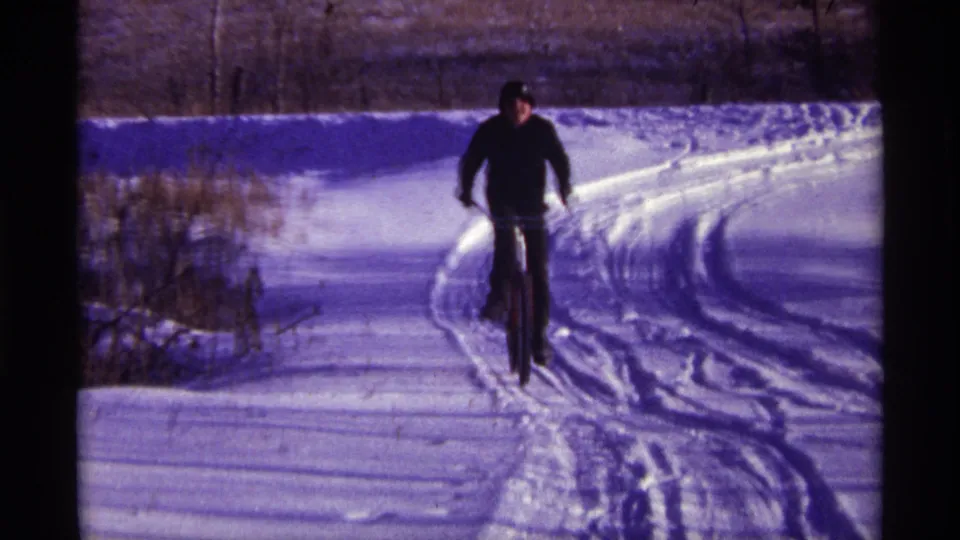 A bundled cyclist approaches along a curved snow track in Chicago home-movie footage from 1968.
