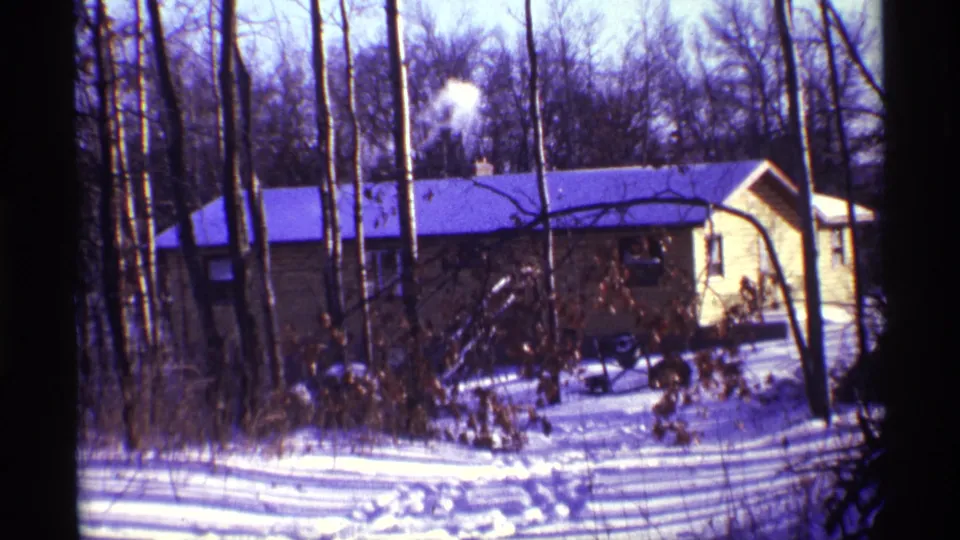 1968 Chicago 8mm frame showing a yellow house with a smoking chimney among bare trees and snow.