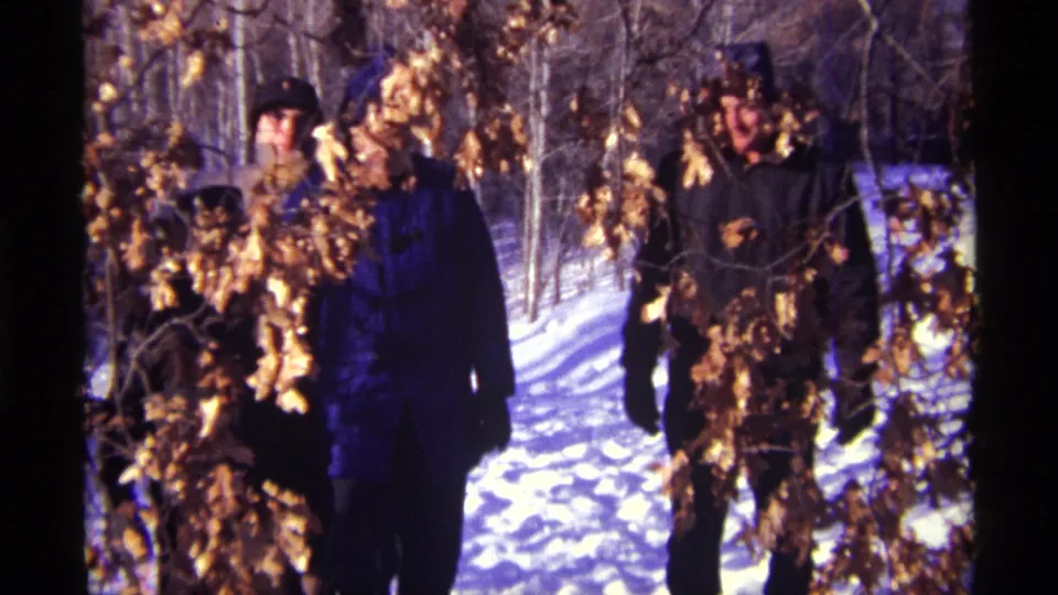 Several bundled people in winter coats and hats walk toward the camera through snowy Chicago woods.