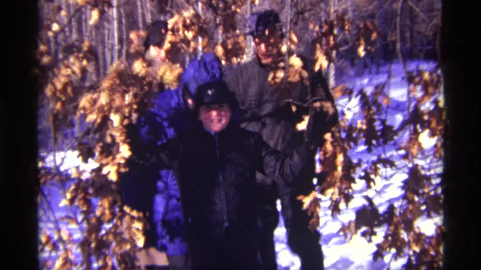 1968 Chicago-area 8mm frame showing several bundled people walking through snow in a wooded setting.