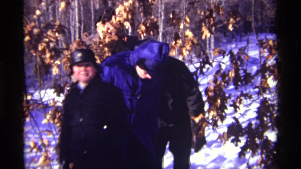 1968 Chicago-area home-movie frame with bundled figures in snow, including a person in a bright blue hooded coat.