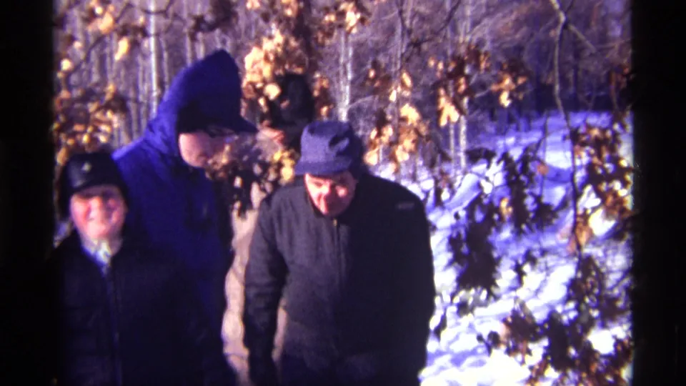 1968 Chicago-area 8mm frame showing bundled people in coats and hats moving through a snowy wooded area.