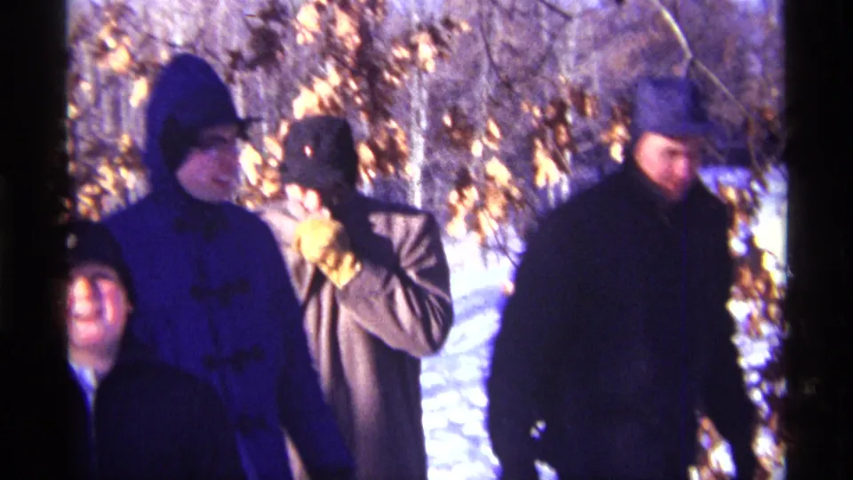 1968 Chicago-area home-movie frame of bundled people in snow, framed by bare trees and brown winter leaves.