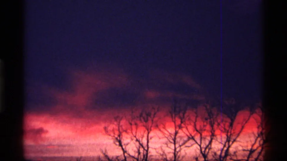 1968 Chicago-area 8mm frame showing a low orange sunset band beneath purple clouds and leafless tree silhouettes.