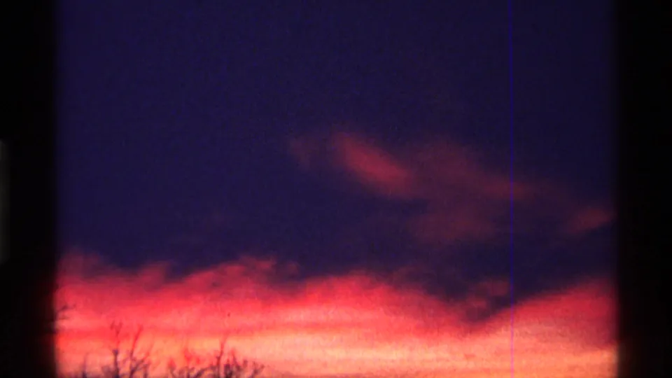 1968 Chicago-area 8mm frame with dark purple cloud mass, bright orange horizon light, and faint tree silhouettes below.