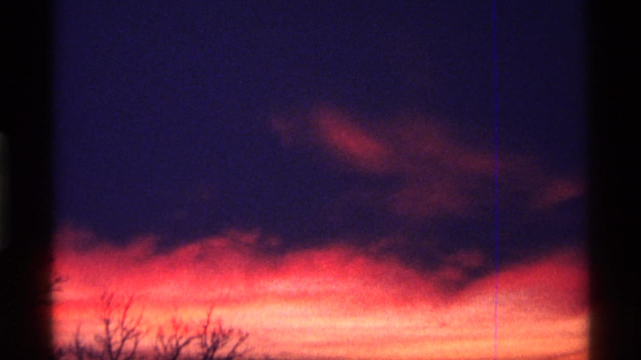 1968 8mm frame from Chicago metadata showing a saturated sunset sky with dark brush silhouettes and visible film borders.
