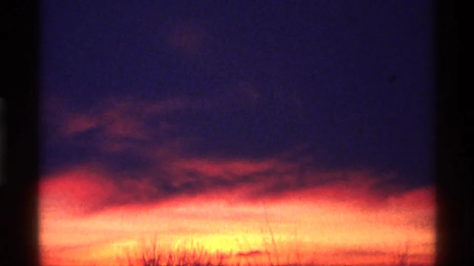 1968 8mm home-movie frame showing a vivid sunset gradient, faint clouds, and silhouetted trees or brush along the lower frame.