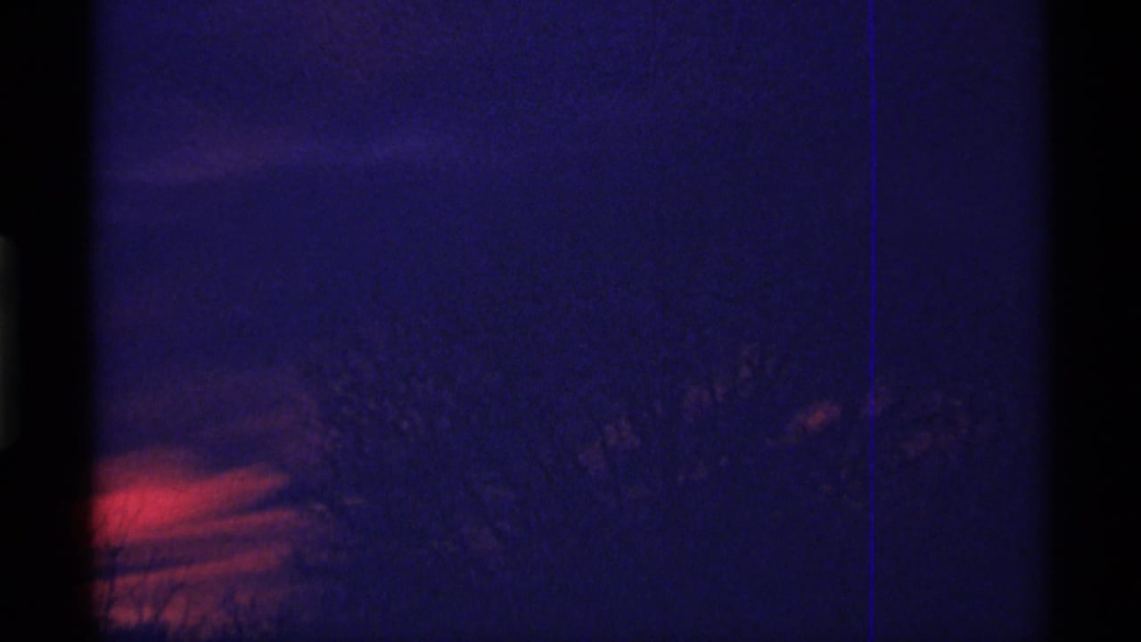 1968 Chicago 8mm frame showing a dark blue evening sky, red-orange horizon glow, and faint silhouetted tree branches.