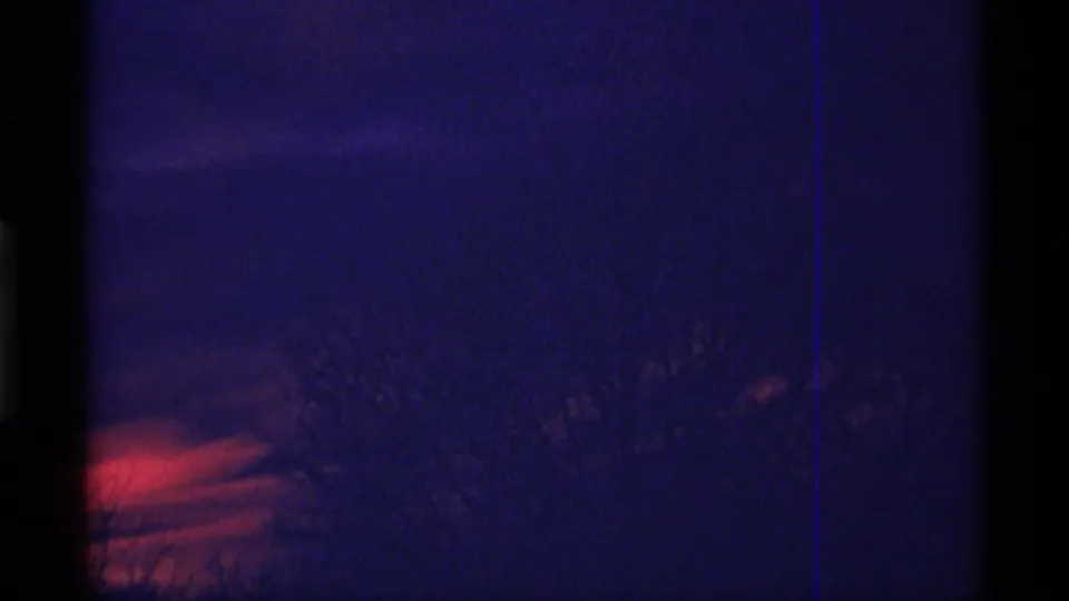 1968 Chicago 8mm frame showing a dark blue evening sky, red-orange horizon glow, and faint silhouetted tree branches.