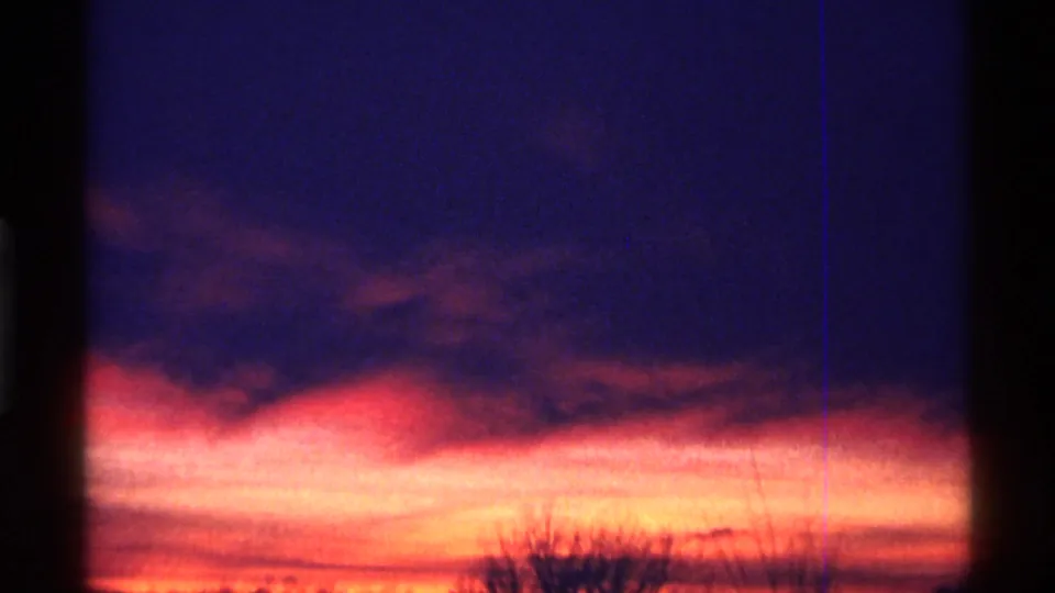 1968 Chicago 8mm frame with a bright orange-red horizon, dark cloud band, and black tree silhouettes at dusk.