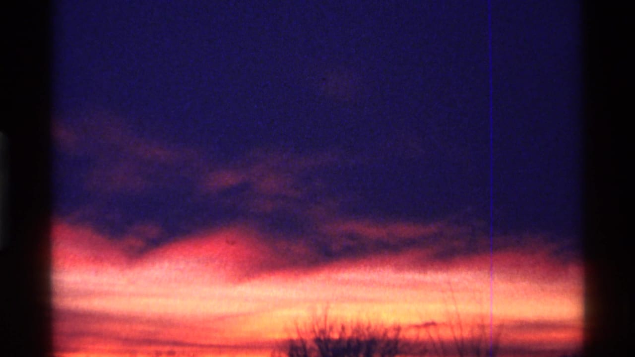 Purple and orange sunset sky with dark clouds and faint tree silhouettes.
