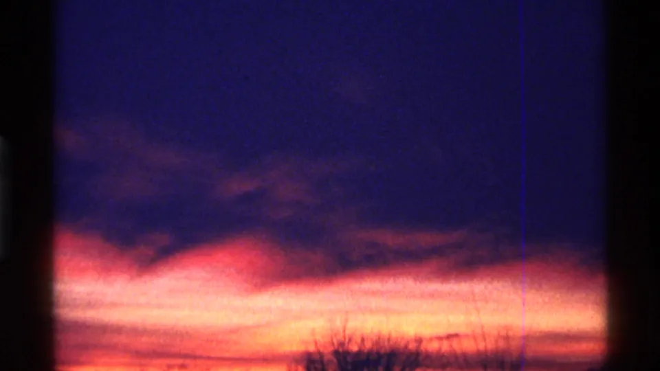 1968 Chicago 8mm frame with a vivid orange sunset beneath purple clouds, bordered by dark film-edge shadows.