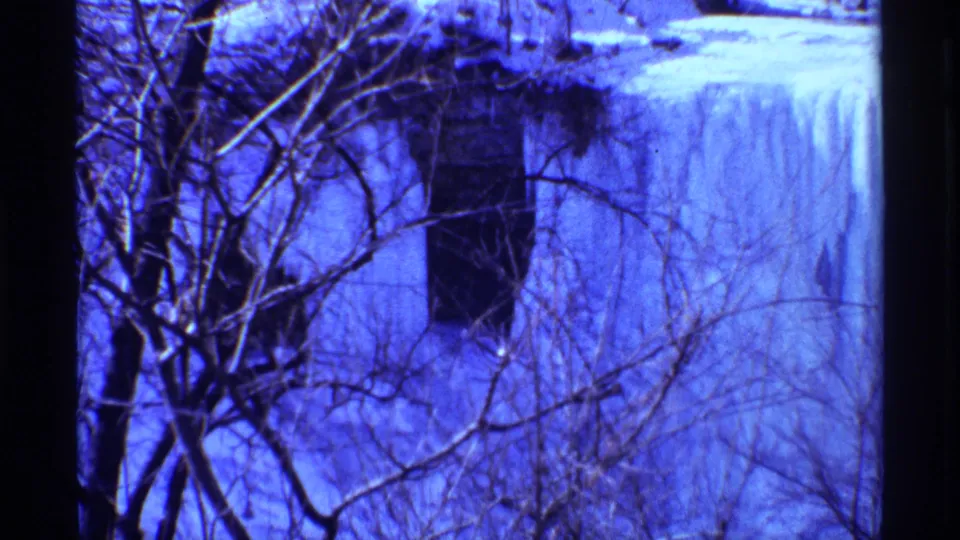 1968 Chicago-area winter frame showing a frozen waterfall, snow-covered ground, leafless trees, and cool blue 8mm color shift.