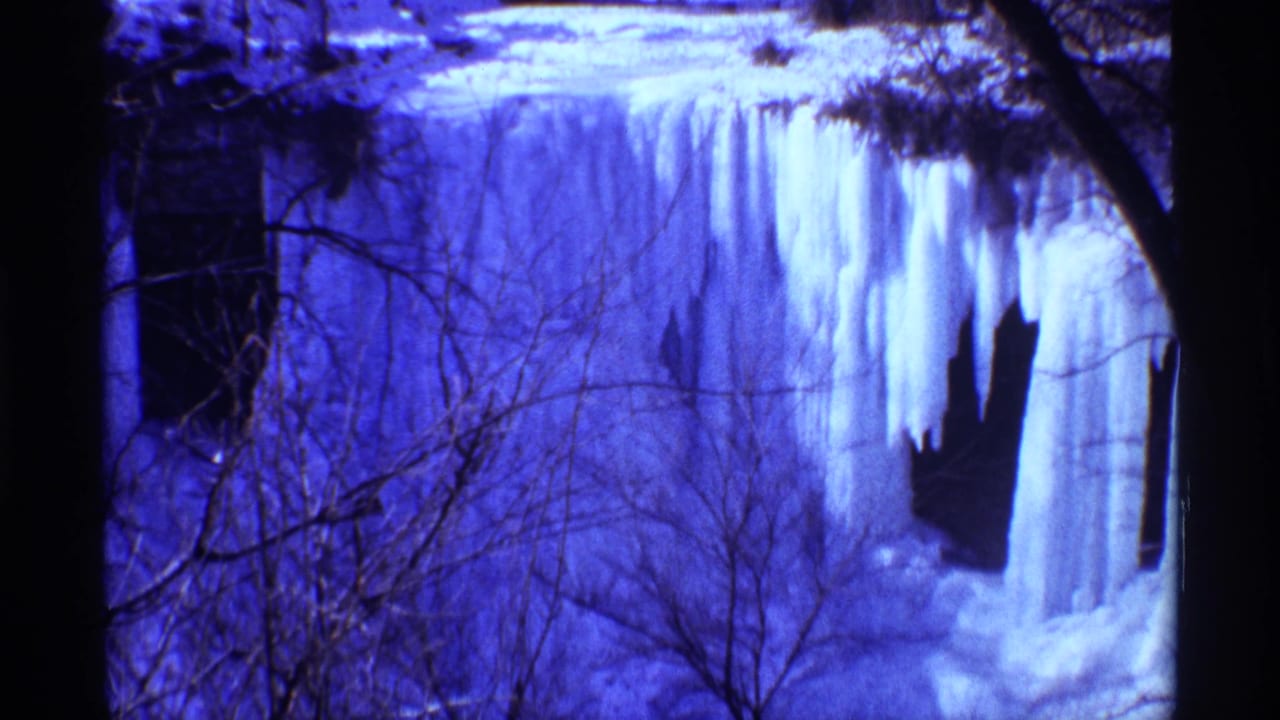 Frozen waterfall framed by dark tree trunks and bare branches.