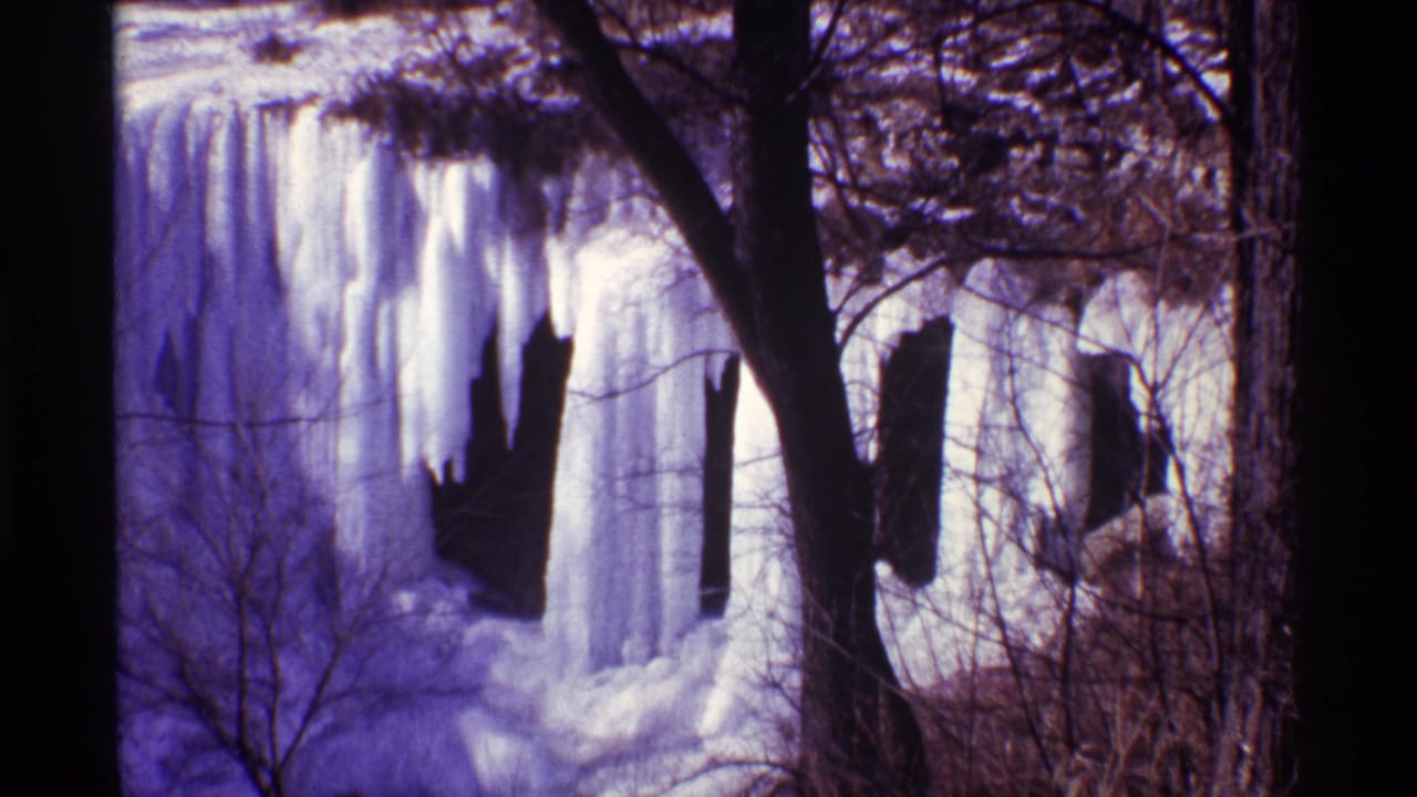 1968 Chicago home-movie frame showing a frozen waterfall, hanging icicles, bare branches, and dark rock openings.