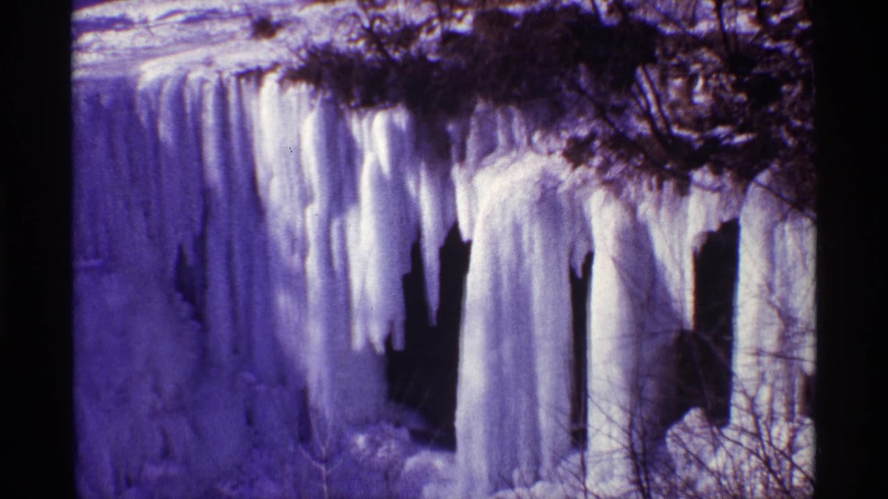 Large icicles hang from a rocky frozen waterfall with bare branches across the top.