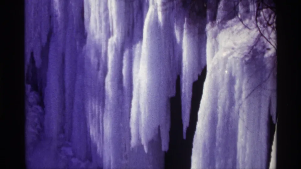 Close 1968 8mm view of white and purple-blue ice columns hanging over dark gaps in the frozen waterfall.