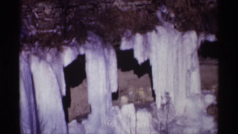 Wider 1968 8mm view near Chicago showing heavy icicles over dark rock with ice and snow collected at the base.