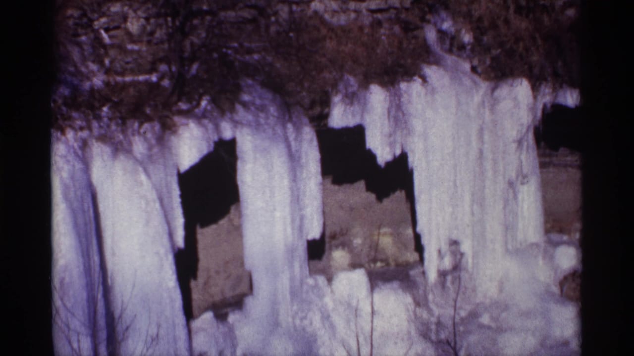 1968 8mm home-movie frame showing heavy icicles and frozen buildup beneath a dark rocky overhang.