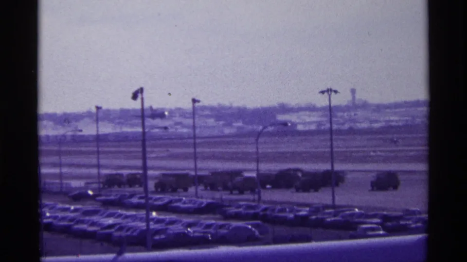 1968 Chicago airport view with rows of vintage cars, light poles, and a distant tarmac under a pale sky.