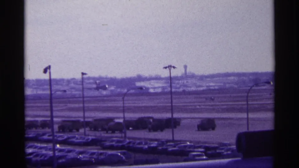 1968 Chicago airport view with a commercial airplane beginning takeoff beyond parked cars and service vehicles.