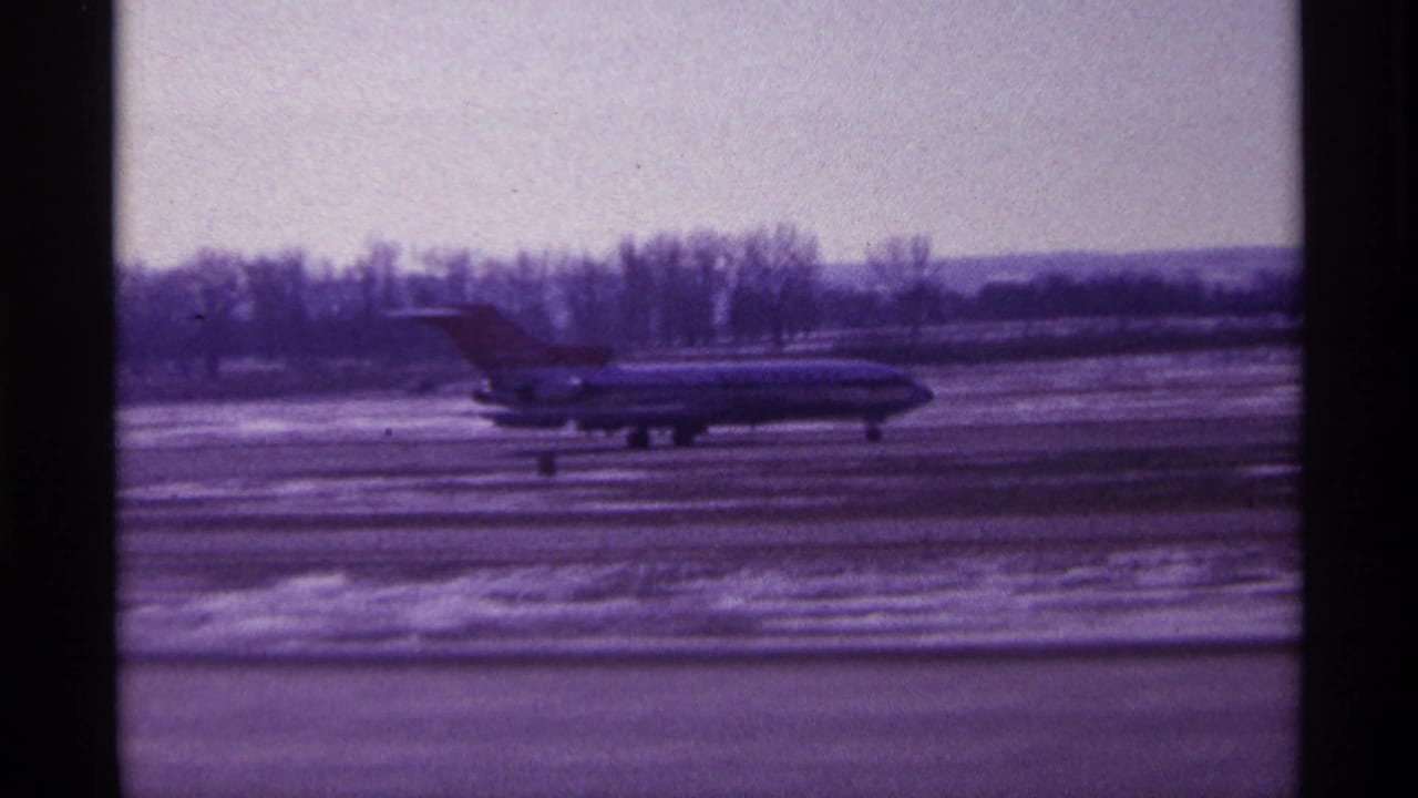 Commercial jetliner taxiing across a snowy airport tarmac behind dark vertical borders.