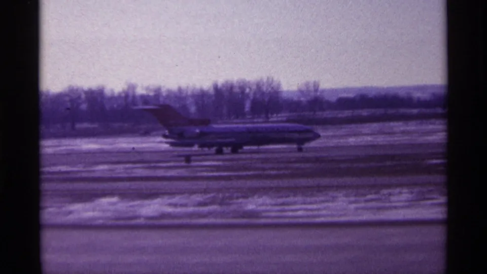 1968 Chicago home-movie frame of a jetliner moving across a snow-lined airport tarmac under a pale winter sky.