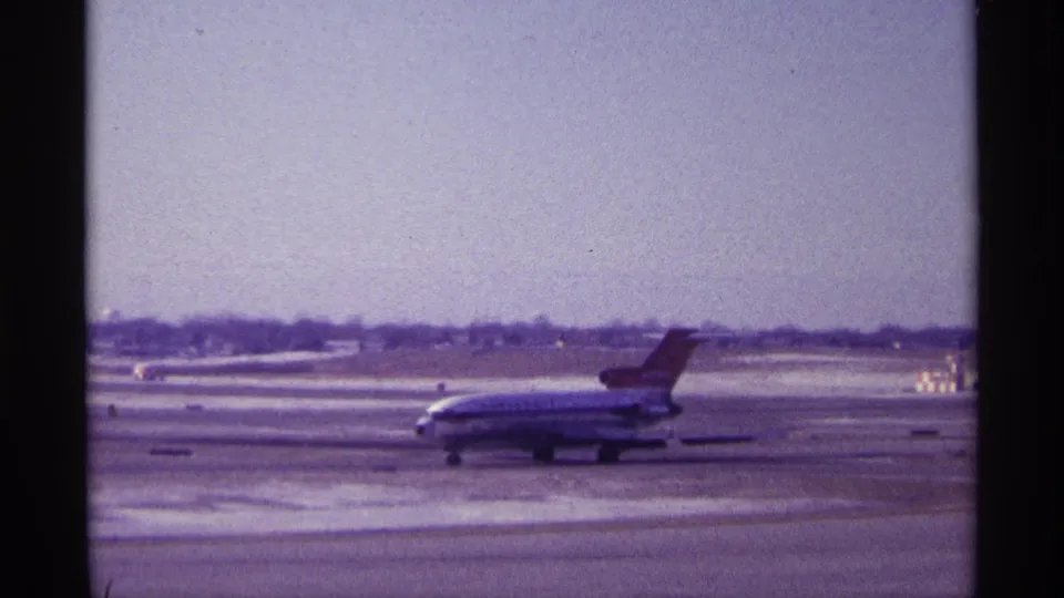 1968 Chicago home-movie still of a jetliner taxiing on airport pavement beside snow-covered ground.