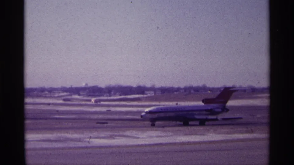 1968 Chicago winter airport frame with a commercial jetliner taxiing across the tarmac in aged 8mm color.