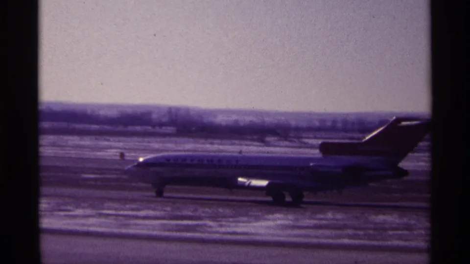 Northwest Airlines aircraft passes across the frame in a 1968 Chicago airport scene with snow on the ground.