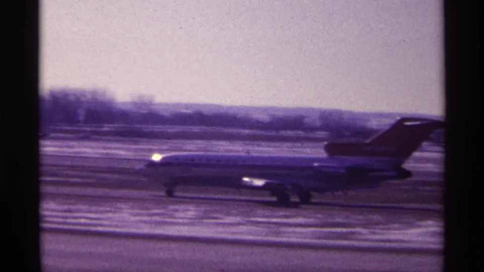 Soft 8mm frame of a Northwest Airlines jet taxiing through a snowy Chicago airport setting in 1968.