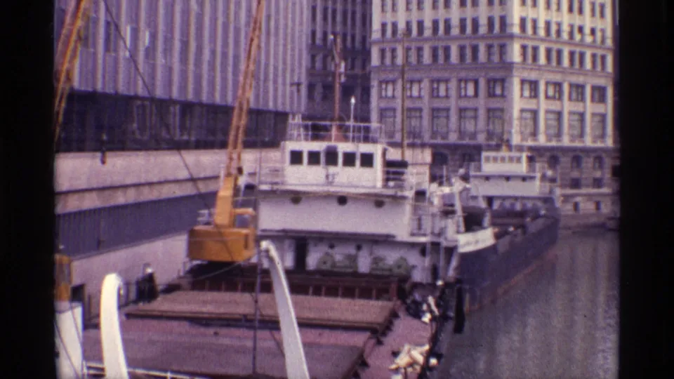 Chicago riverfront view from 1968 showing a docked barge with a yellow crane, tall waterfront buildings, and small people on the vessel.