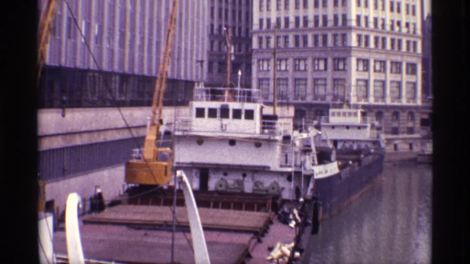 1968 Chicago river scene with a barge, crane, boat cabin, river channel, waterfront architecture, and small people near the deck.