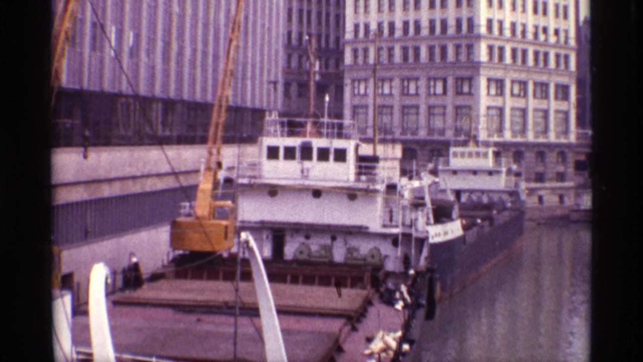 1968 Chicago dock scene with a cargo ship, yellow crane, water channel, and downtown buildings visible from an elevated home-movie angle.