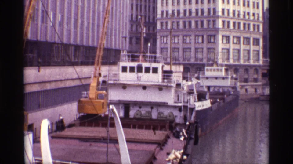 1968 Chicago dock scene with a cargo ship, yellow crane, water channel, and downtown buildings visible from an elevated home-movie angle.
