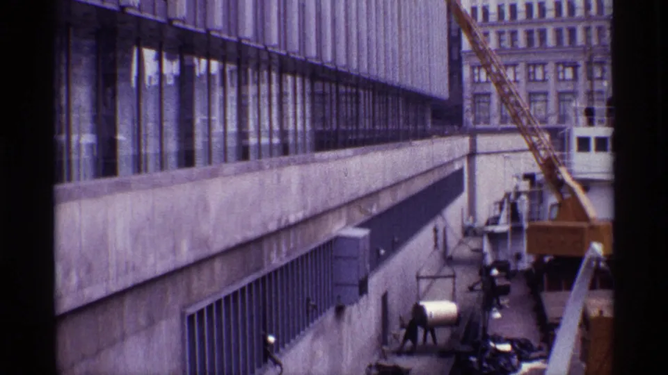 The 8mm frame shows dock workers, a yellow crane, suspended cylindrical cargo, and a ship beside a Chicago waterfront building.