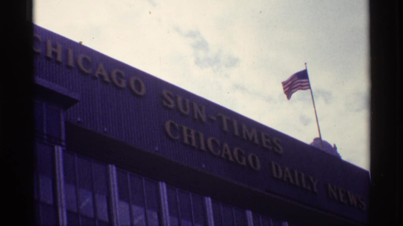 1968 Chicago 8mm frame showing newspaper mastheads on a building facade with an American flag against the sky.