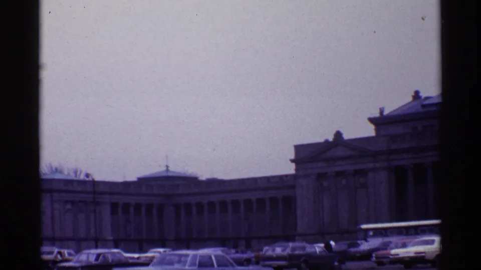 1968 Chicago home-movie frame with a wide view of the grand columned building, clustered cars, a bus, and tiny pedestrians near the street.