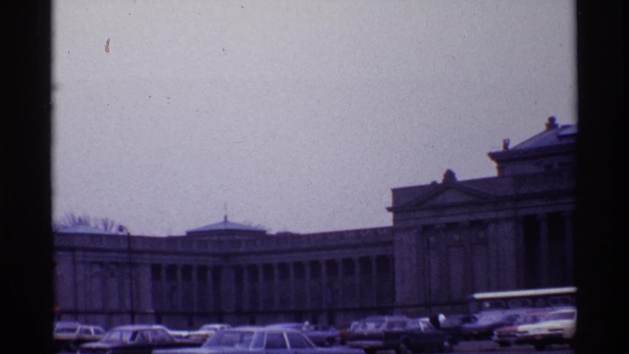Classical domed building with parked cars and a white bus along the street.