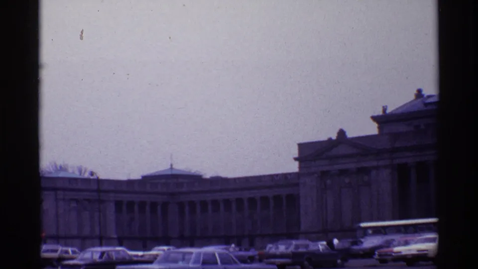 1968 Chicago home-movie frame showing a large classical building, curbside cars, and a white bus under an overcast sky.