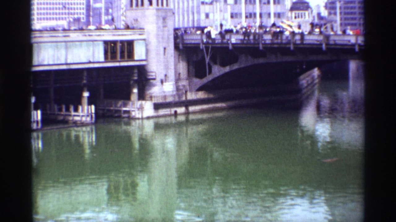 1968 Chicago river view with pedestrians on a bridge, masonry bridge structures, downtown buildings, and reflections on the water.